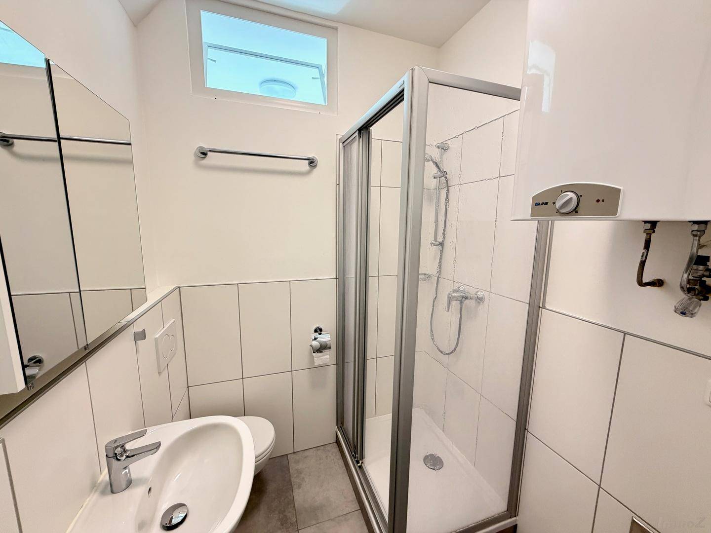 Helles Badezimmer mit Duschkabine, Waschbecken und praktischem Spiegelschrank.