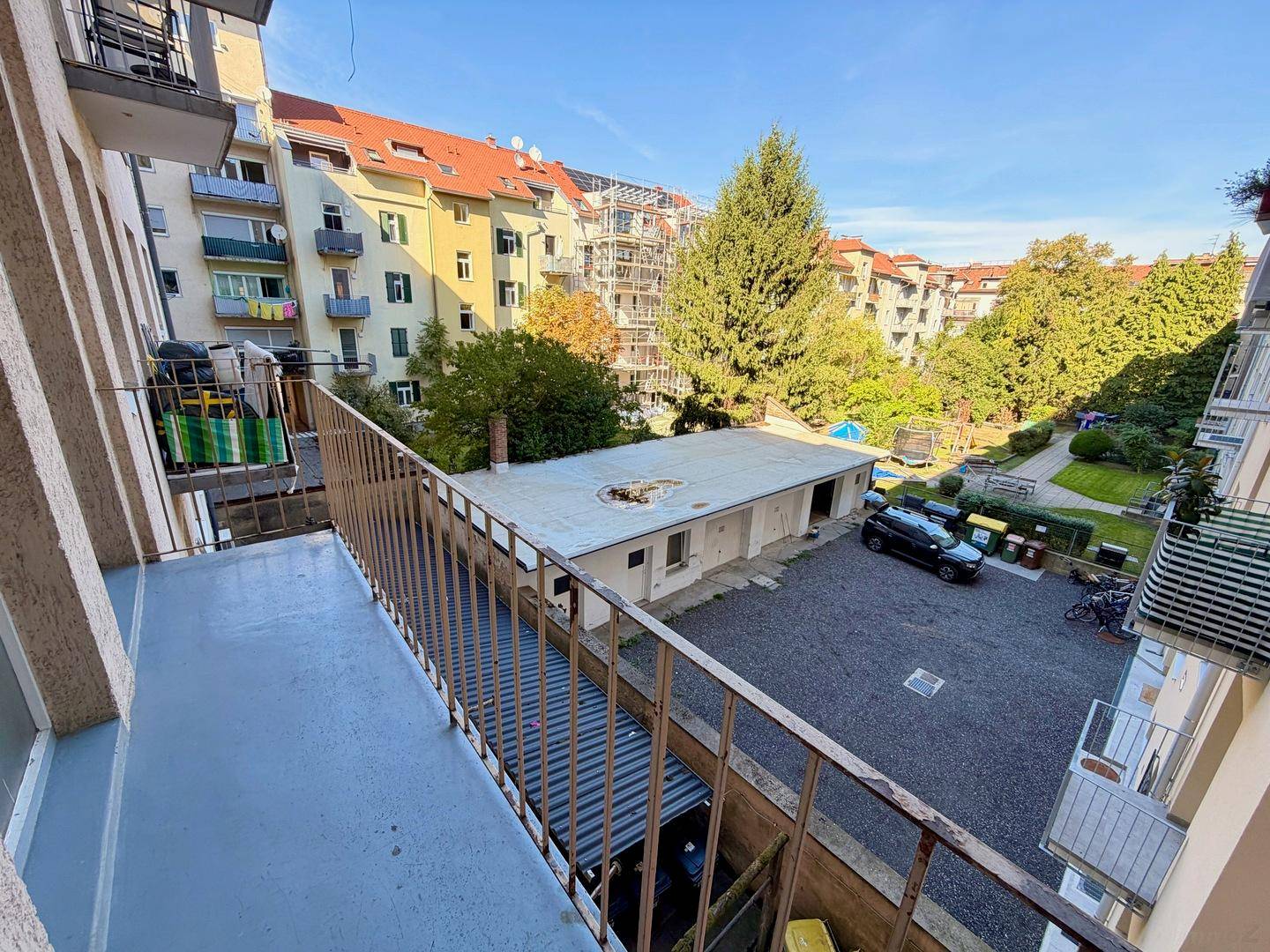 Balkon mit Blick auf den Innenhof, umliegende Gebäude und grüne Bäume.