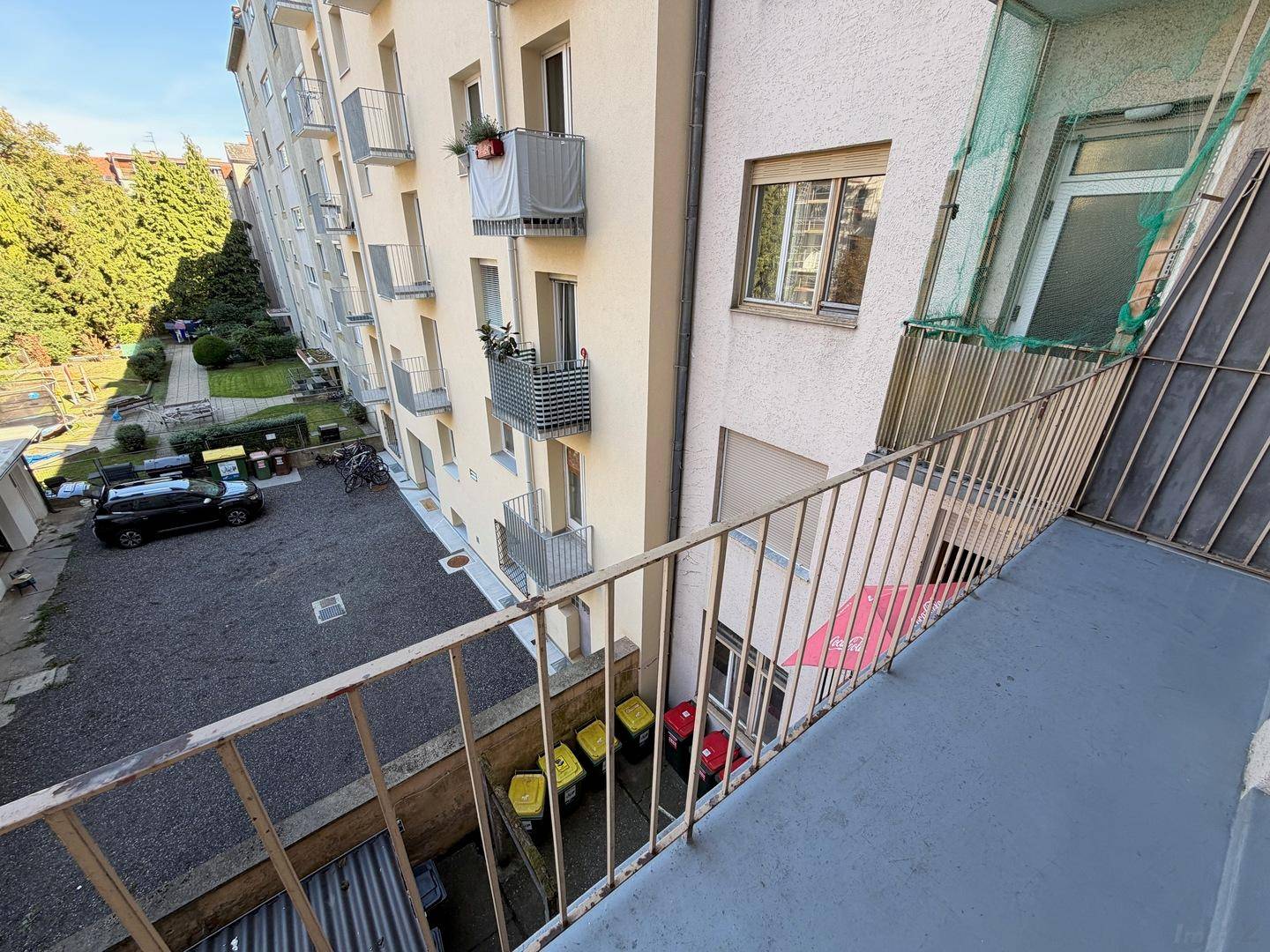 Sonniger Balkon mit Aussicht auf den begrünten Innenhof und die Nachbargebäude.
