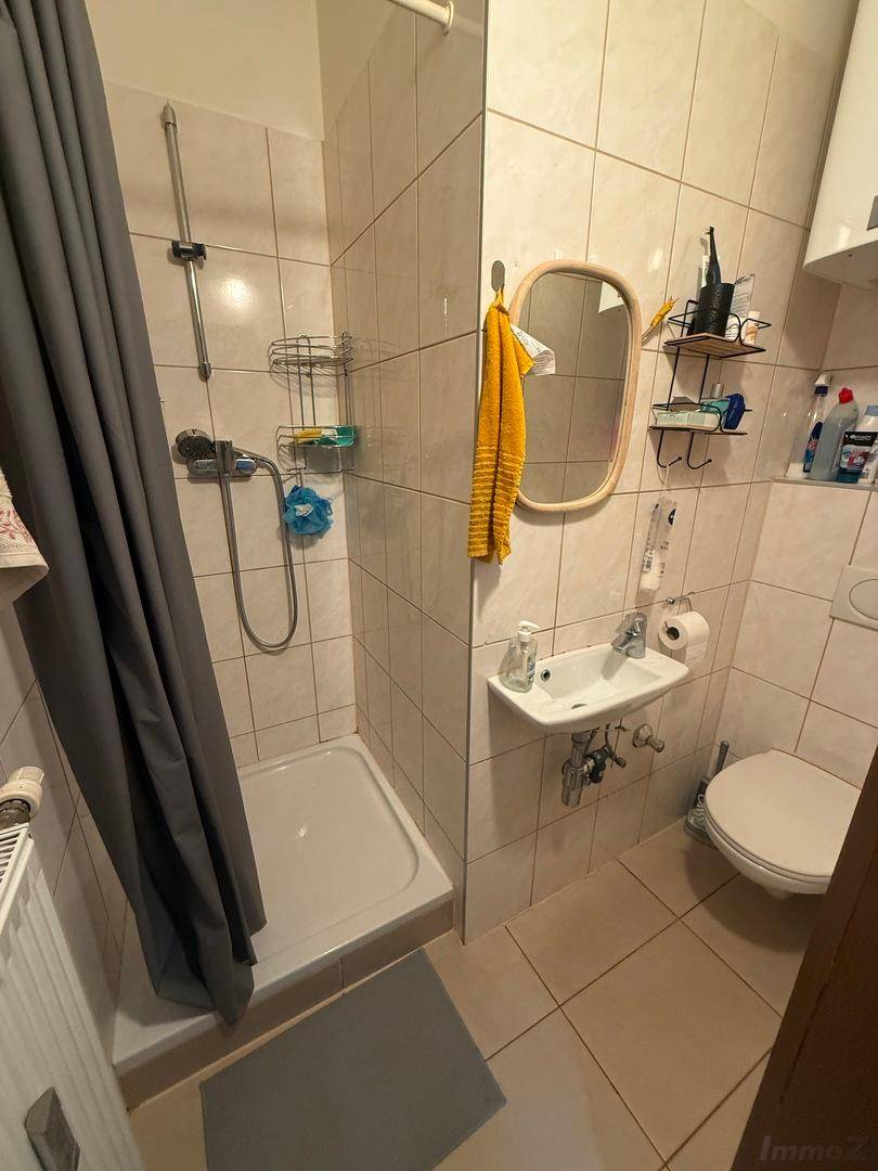 Funktionales Badezimmer mit Duschkabine, WC, kleinem Waschbecken und hellen Fliesen.
