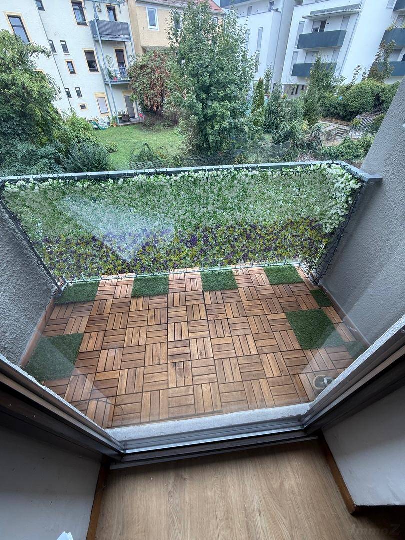 Gemütlicher Balkon mit Holzbodenfliesen und grüner Sichtschutzwand, bietet Blick ins Grüne.