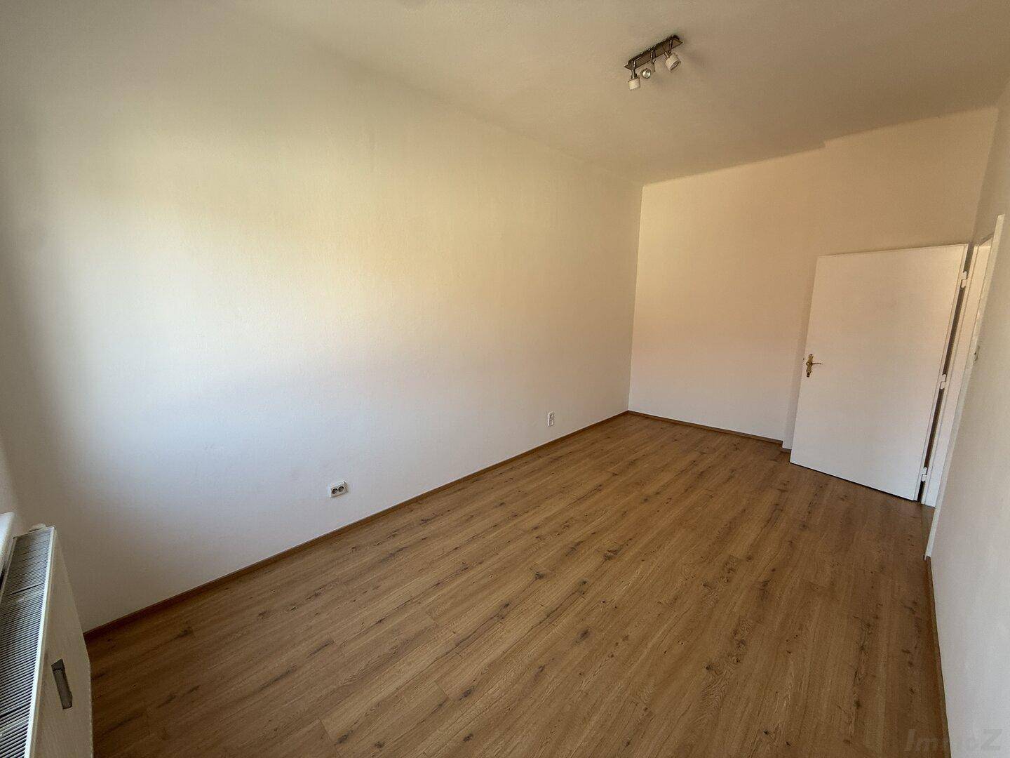 Leeres Zimmer mit Laminatboden und weiß gestrichenen Wänden, bietet viel Potenzial für individuelle Gestaltung.