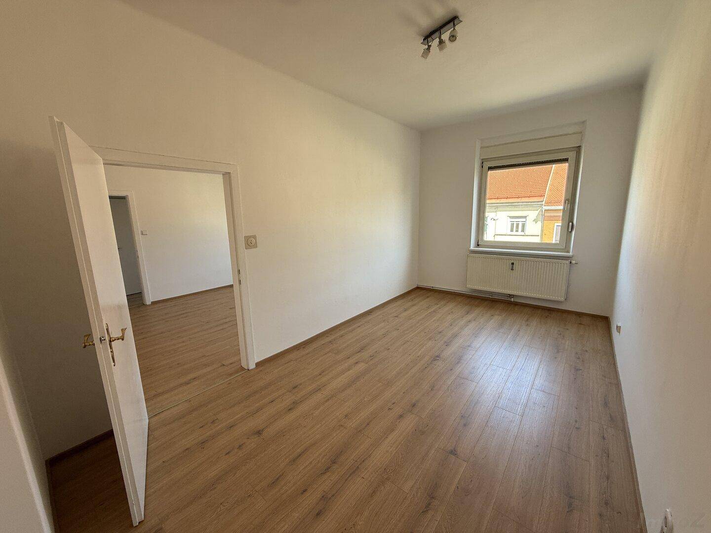 Lichtdurchflutetes Zimmer mit Laminatboden und Fenster, das einen Blick auf die Umgebung bietet.