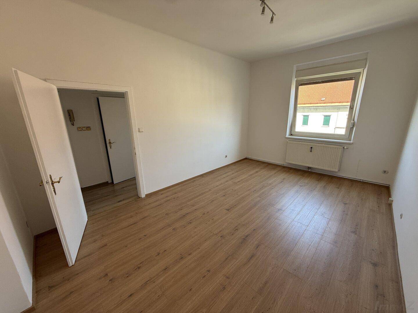 Lichtdurchflutetes Zimmer mit Laminatboden und Fenster, das einen Blick auf die Umgebung bietet.