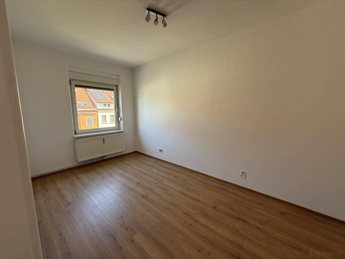 Helles Zimmer mit Laminatboden und weiß gestrichenen Wänden, ideal als Schlaf- oder Wohnbereich.