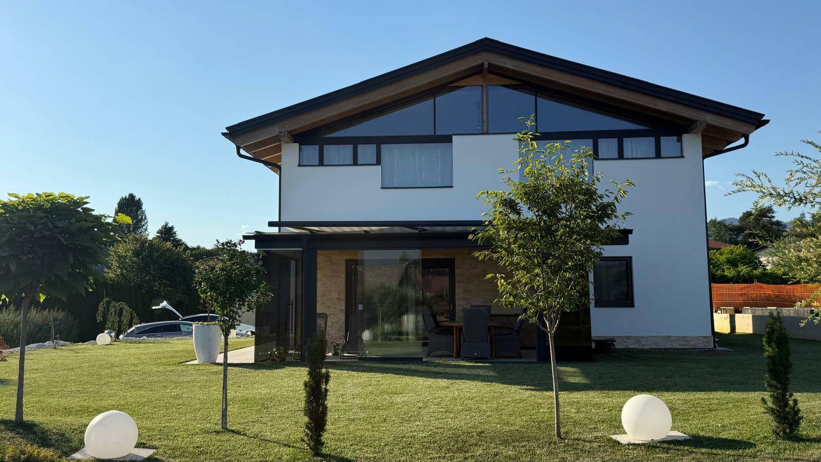 Helles Einfamilienhaus mit gepflegtem Garten und überdachter Terrasse im Sonnenschein.