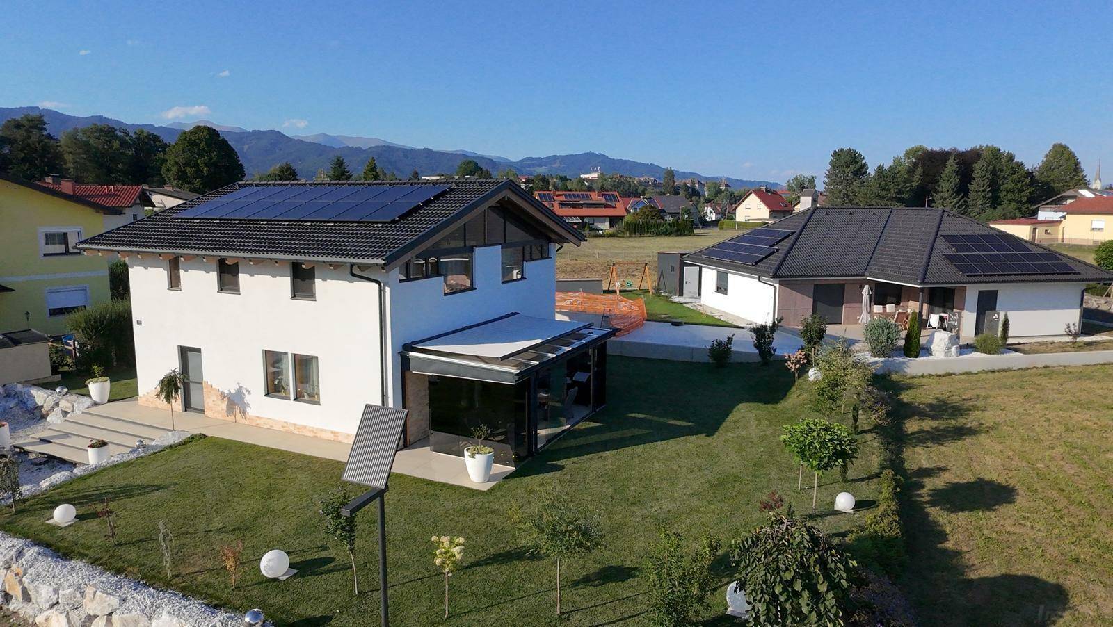 Luftaufnahme von zwei modernen Häusern mit Photovoltaikanlagen und Bergblick.