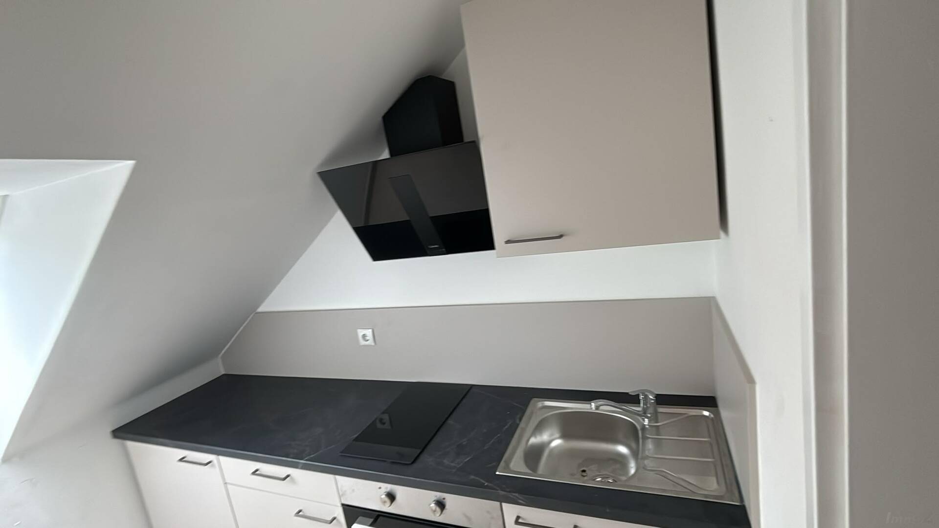 Kompakte Küchenzeile im Dachgeschoss mit Spüle, Kochfeld und Backofen unter der Dachschräge.
