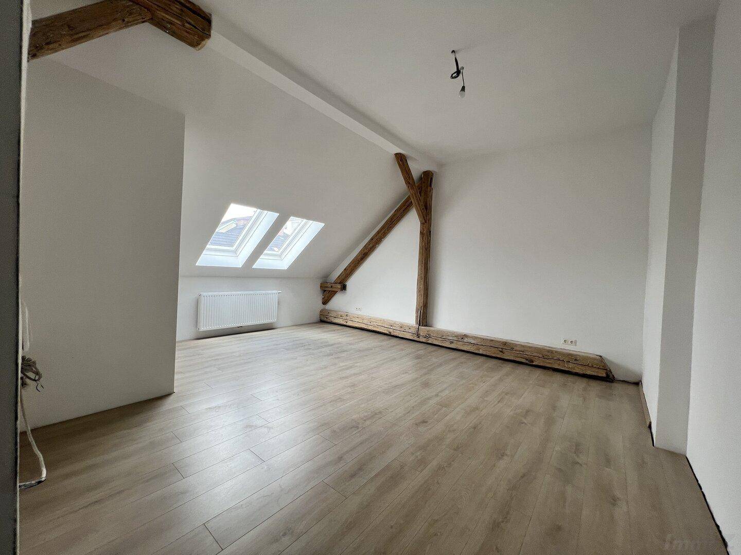 Heller Dachbodenraum mit charakteristischen Holzbalken und schrägen Wänden unter den Dachfenstern.