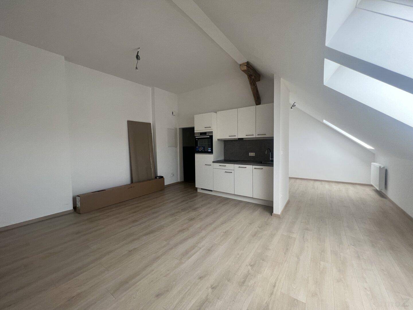 Geräumiger Dachbodenraum mit Küchenzeile, sichtbaren Holzbalken und viel Tageslicht.