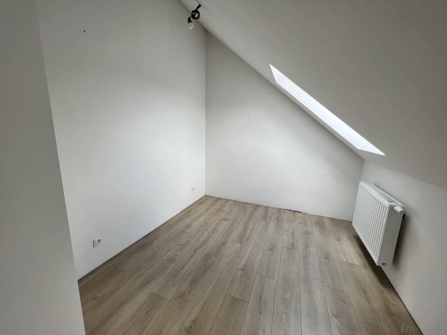 Kleines, helles Zimmer im Dachgeschoss mit Dachfenster und Heizkörper.