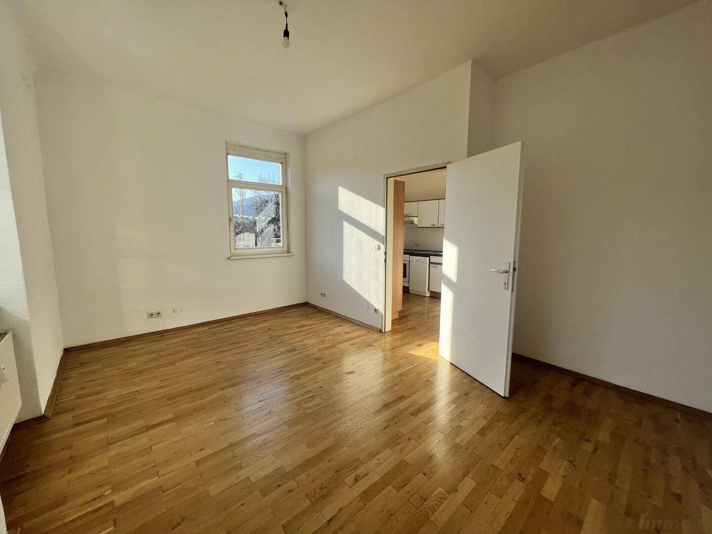Helles Wohnzimmer mit Holzboden und Zugang zur Küche, durchflutet von Sonnenlicht.