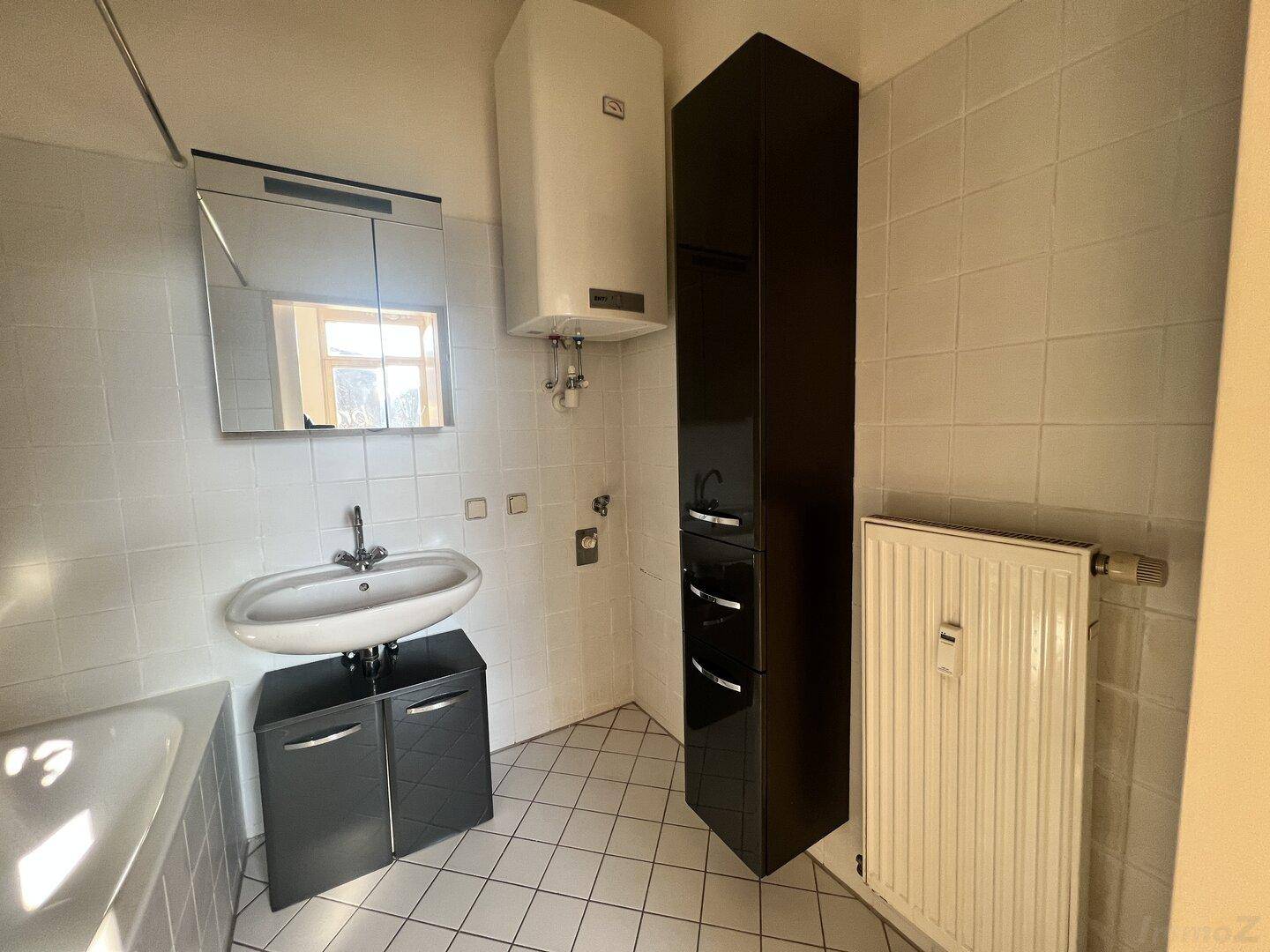 Helles Badezimmer mit Fliesenboden, Waschbecken und Spiegelschrank, inklusive Heizkörper.