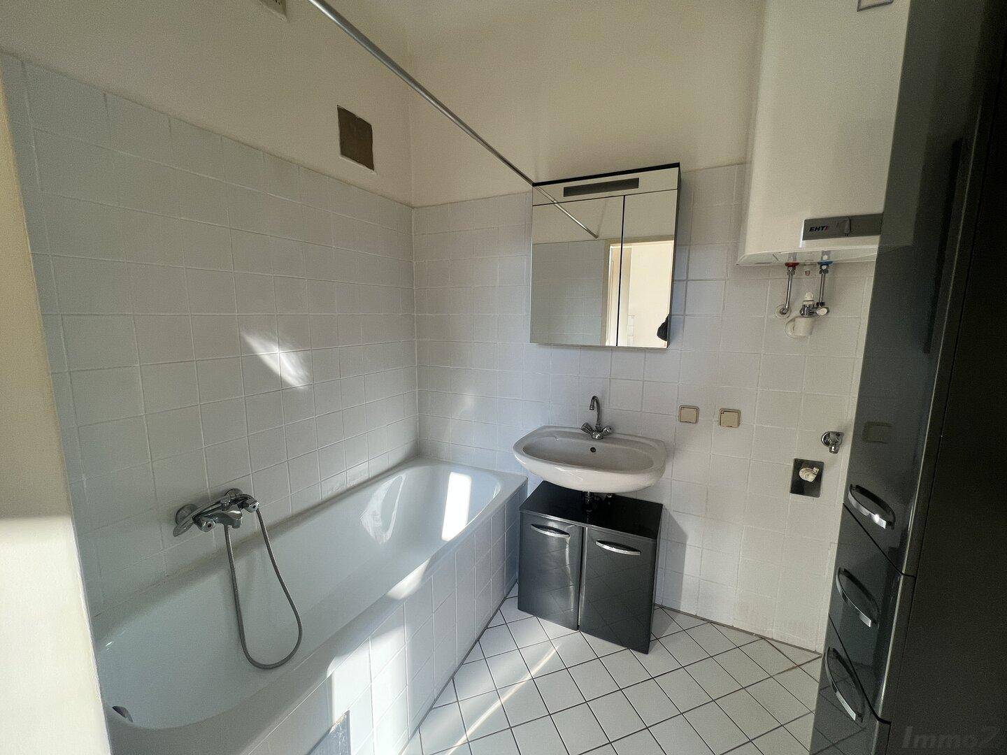 Badezimmer mit Badewanne, Waschbecken und Fliesenboden, ausgestattet mit einem Spiegelschrank.
