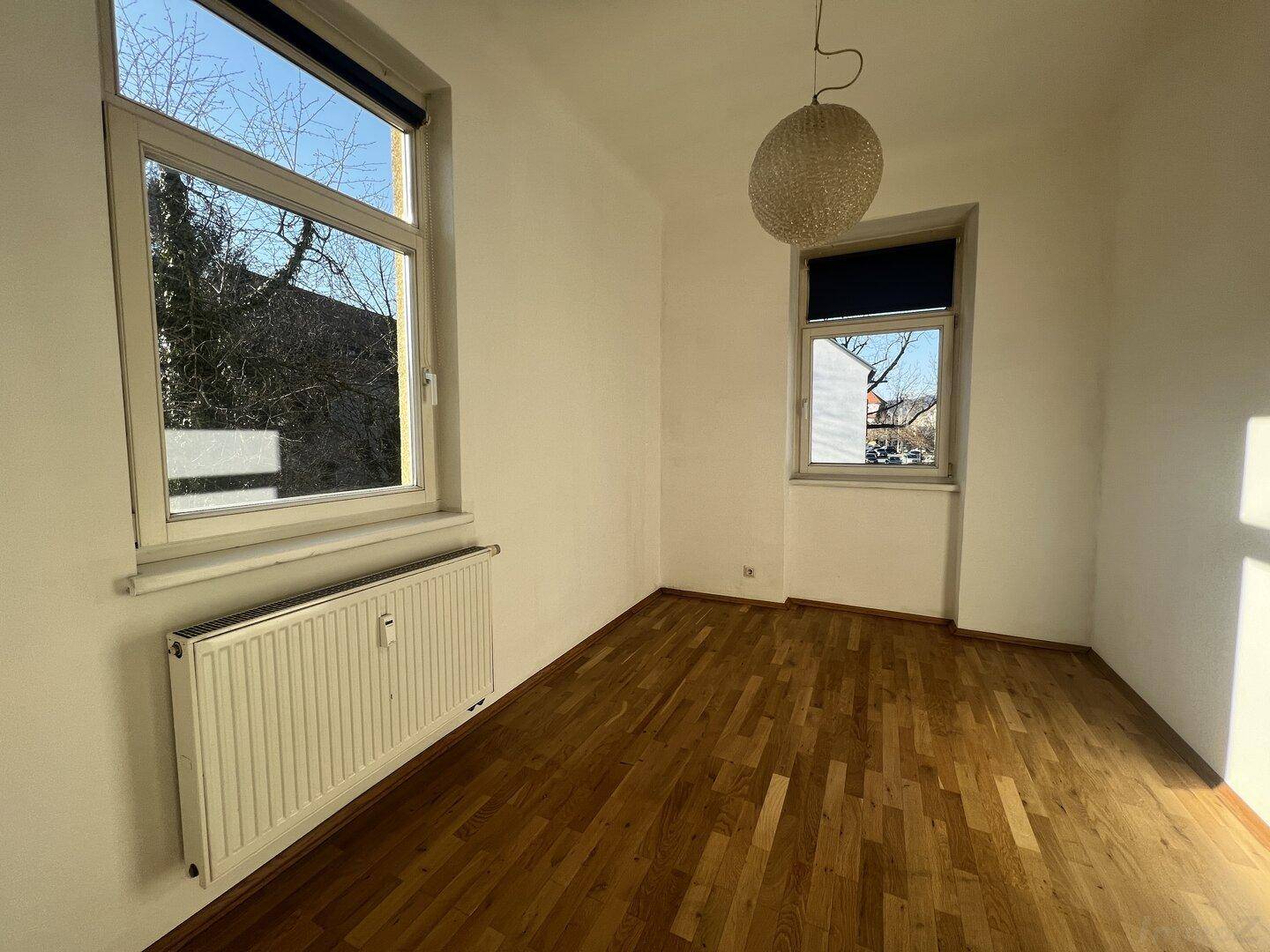Helles Schlafzimmer mit Holzboden und zwei Fenstern, die viel Tageslicht bieten.