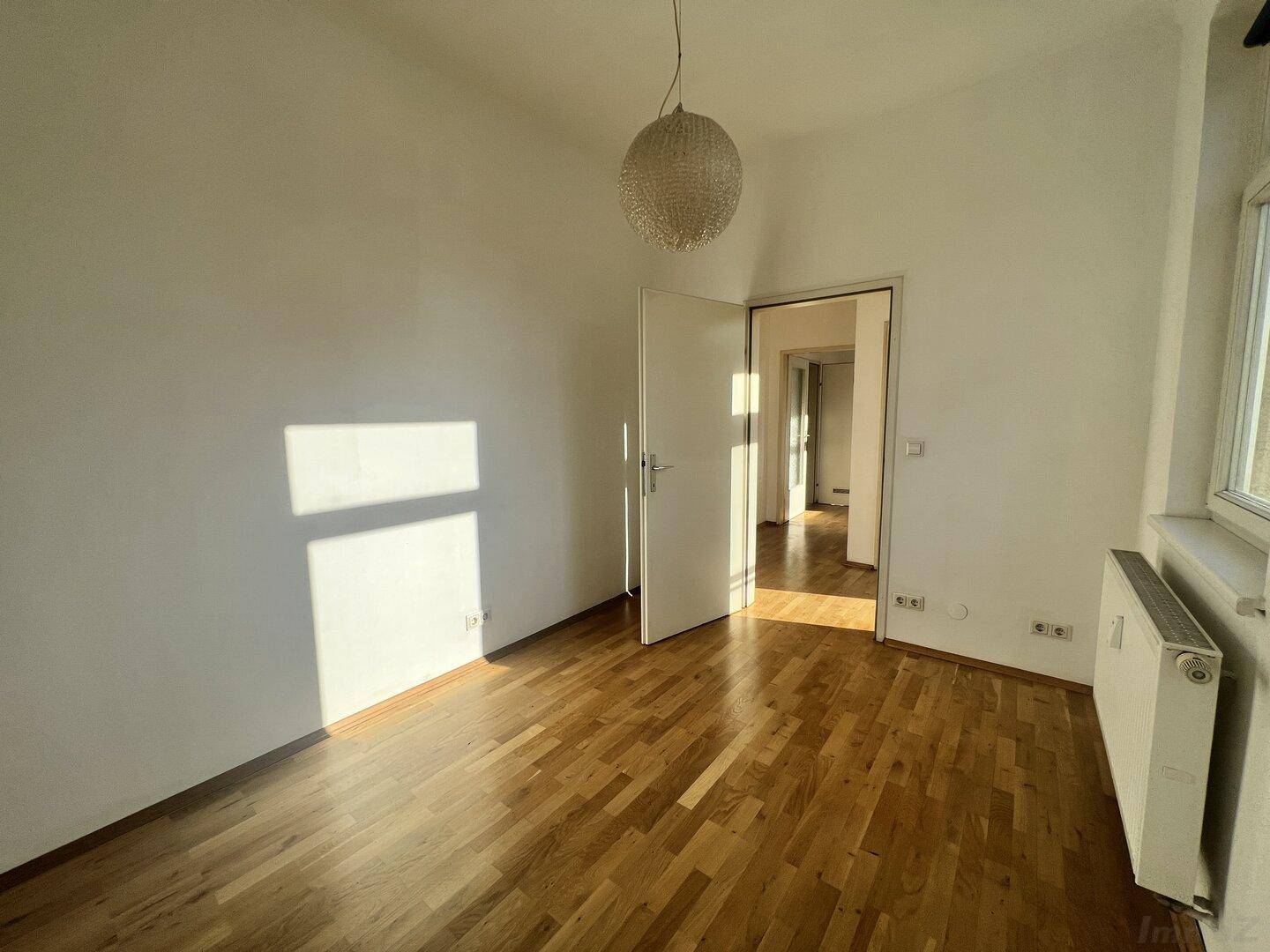 Geräumiges Schlafzimmer mit Holzboden und Zugang zu einem weiteren Raum, hell und einladend.
