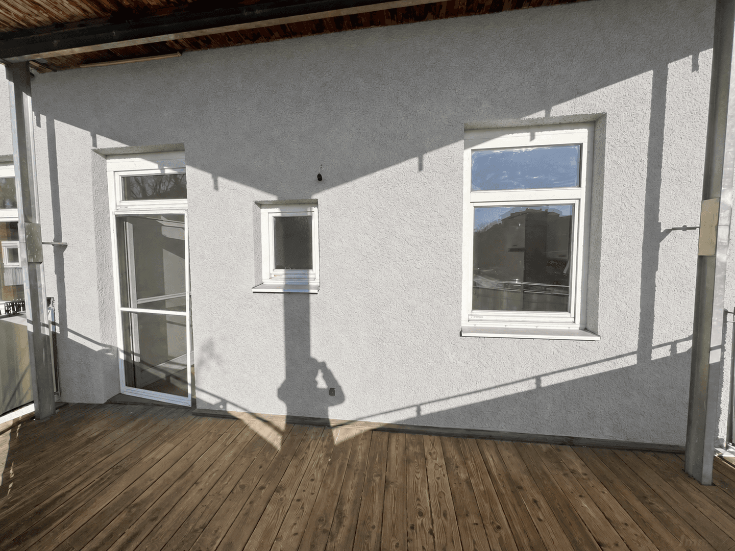 Balkon mit Holzboden und weißer Fassade, die viel Sonnenlicht reflektiert.