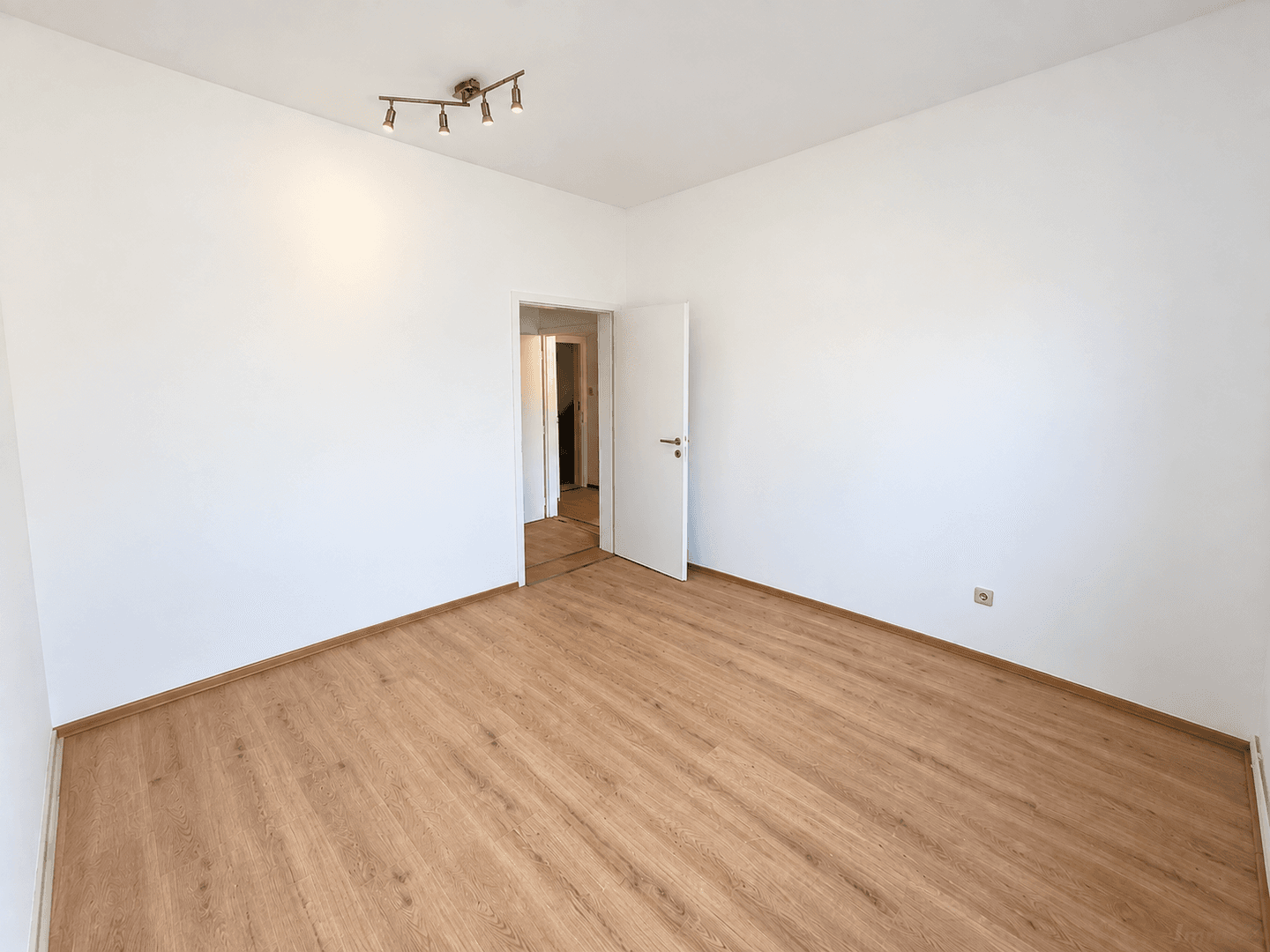 Helles, leeres Zimmer mit Laminatboden und Zugang zu einem weiteren Raum.