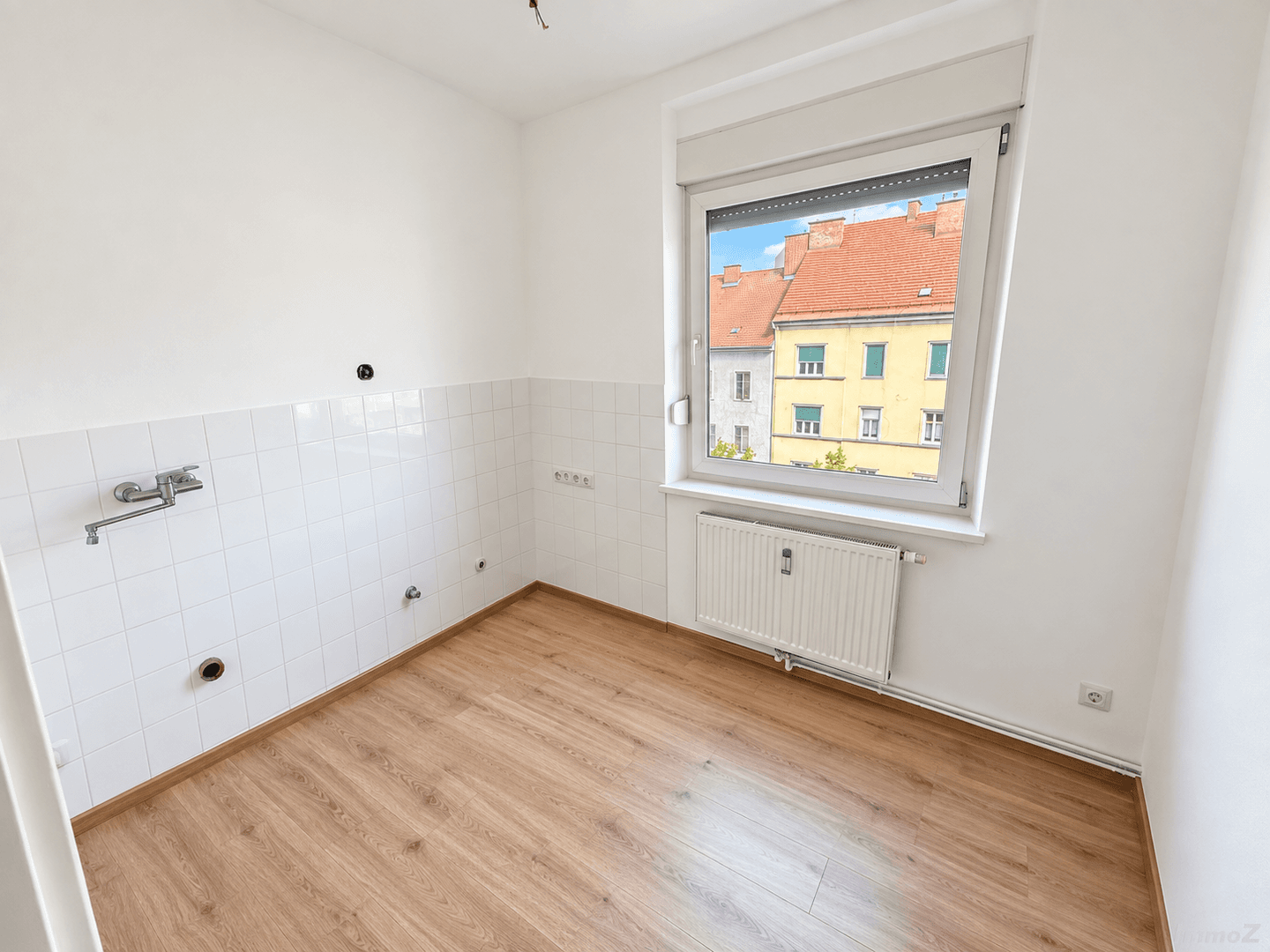 Leerer Küchenbereich mit Fliesenwand, Anschlüssen und Blick aus dem Fenster.