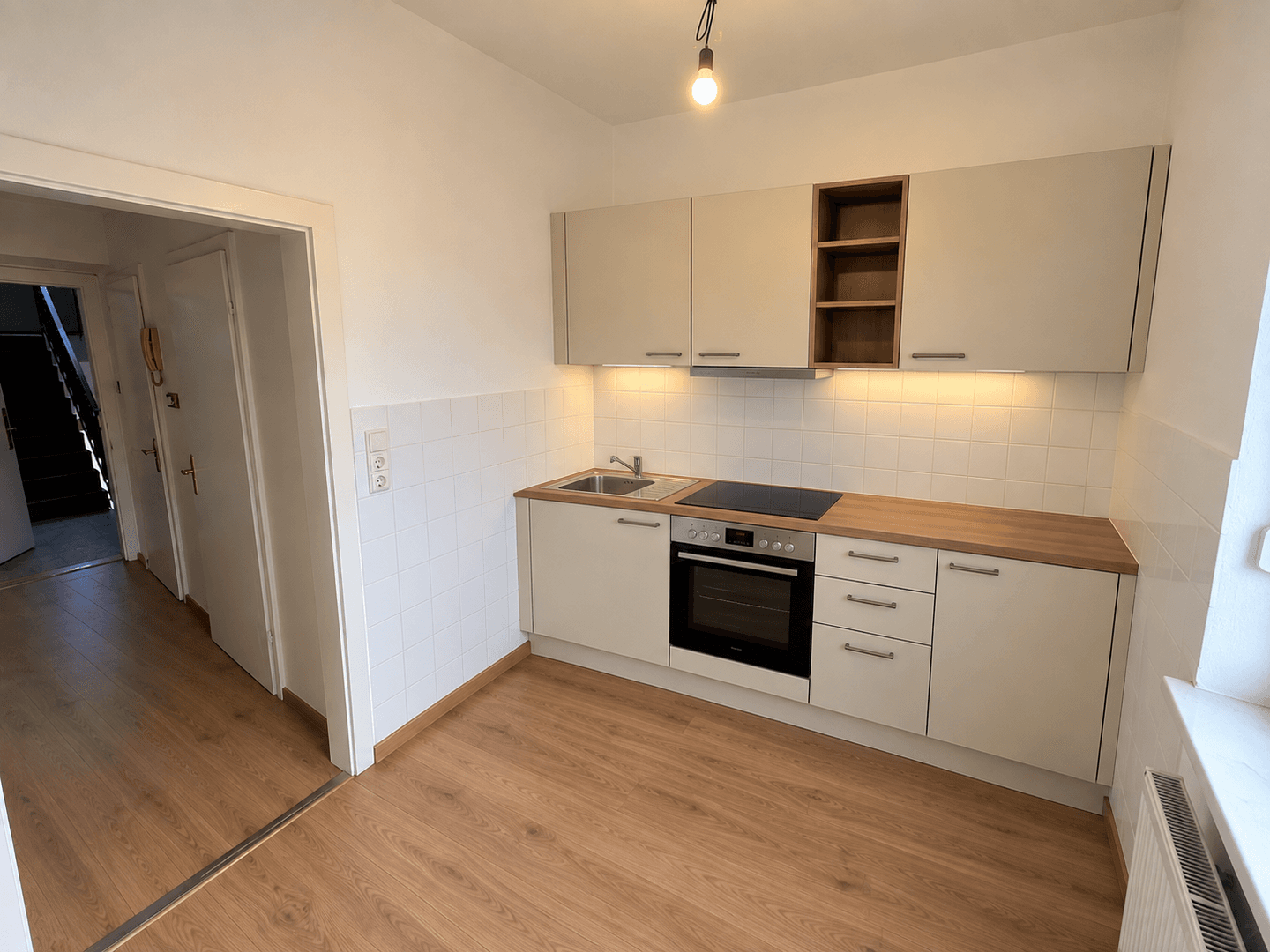 Voll ausgestattete Küche mit beigen Schränken, Holzarbeitsplatte und Zugang zum Flur.