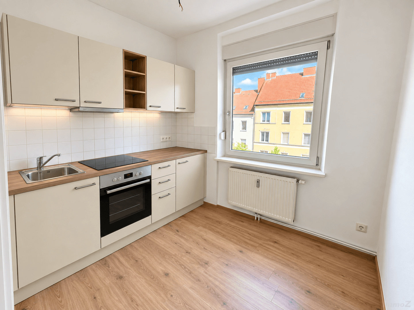 Moderne Einbauküche mit beigen Schränken, Holzarbeitsplatte, Induktionskochfeld und Backofen.