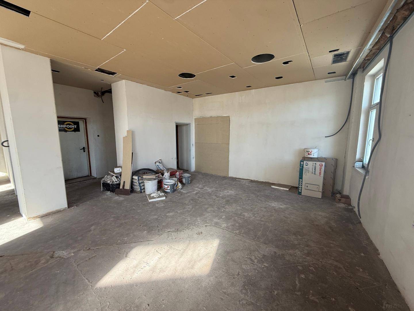 Ecke eines großen Rohbauraums mit Baumaterialien und unfertigen Wänden, bereit für den Innenausbau.