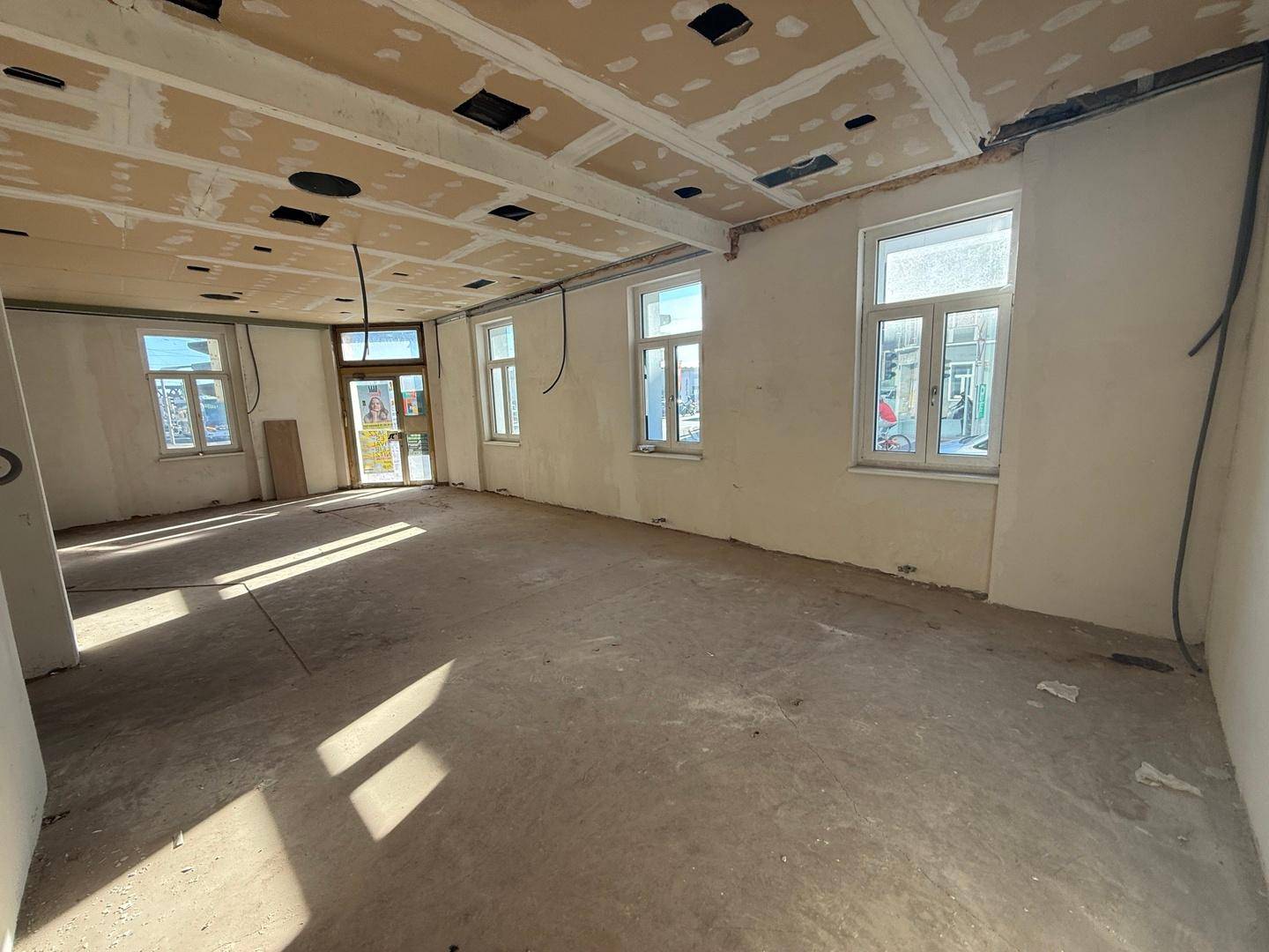 Weiter Blick in den Rohbauraum mit zahlreichen Fenstern und dem Eingangsbereich, der auf Fertigstellung wartet.