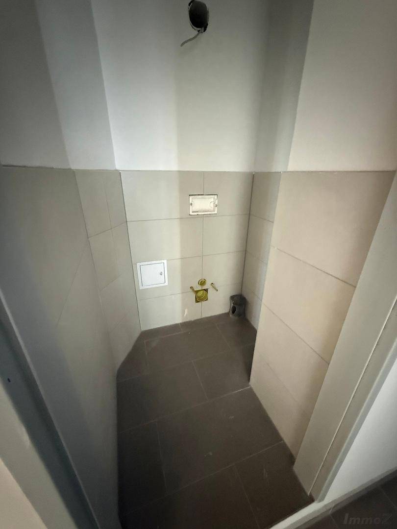 Kleiner, gefliester Raum mit grauen Bodenfliesen und weißen Wandfliesen, vorbereitet für eine Toilette oder Abstellraum.