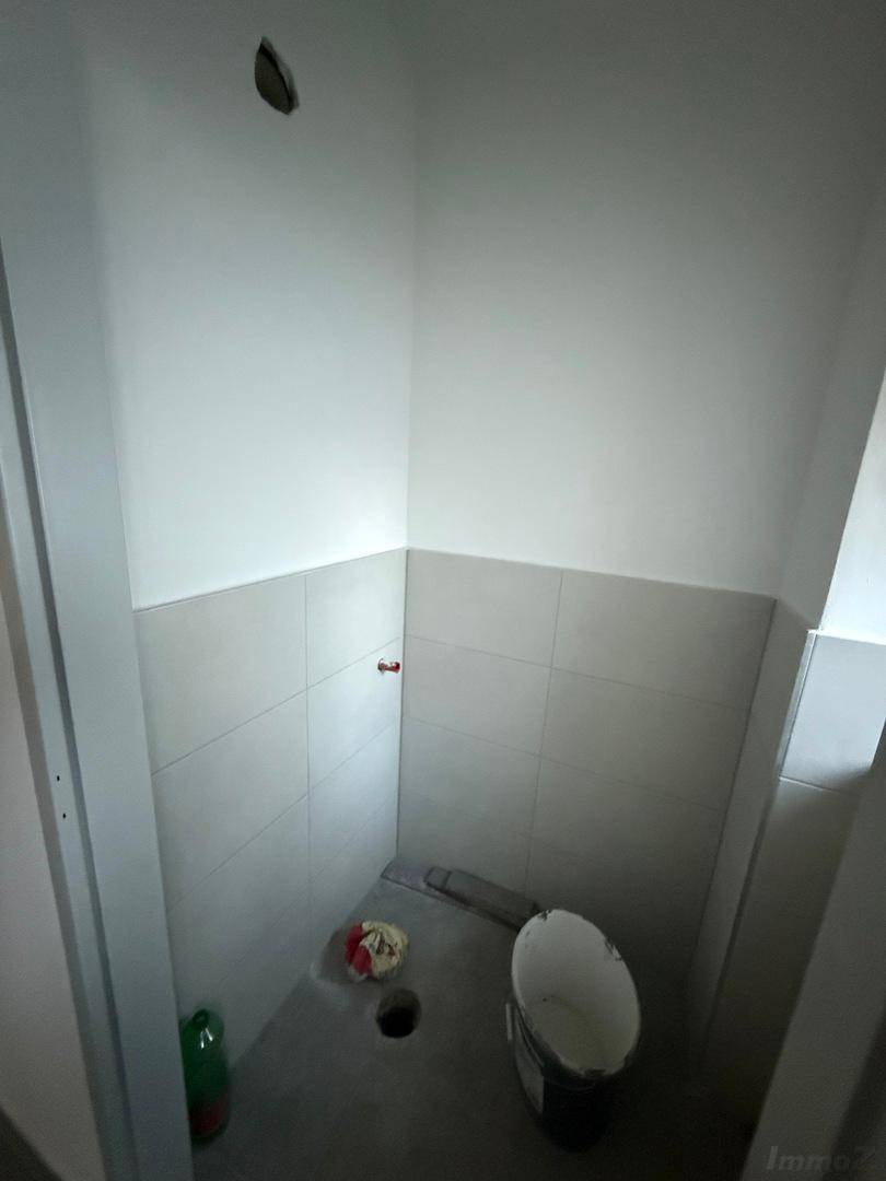 Kleiner, gefliester Raum mit grauen Bodenfliesen und weißen Wandfliesen, vorbereitet für die Installation von Sanitäranlagen.