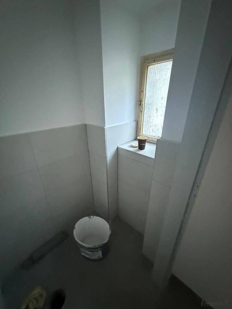 Gefliester Raum mit Fenster, grauen Bodenfliesen und weißen Wandfliesen, ideal für ein Gäste-WC oder Abstellraum.
