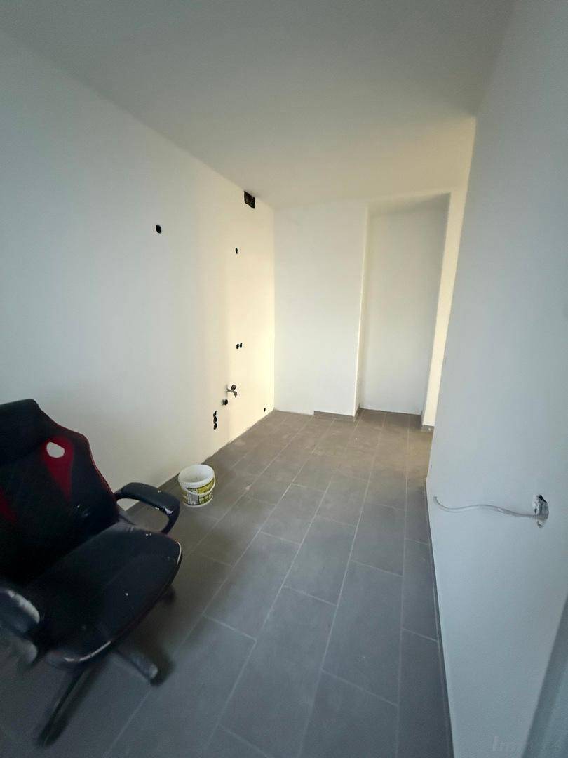 Heller Raum mit grauen Fliesen und weißen Wänden, vorbereitet für die Nutzung als Büro oder Arbeitszimmer.