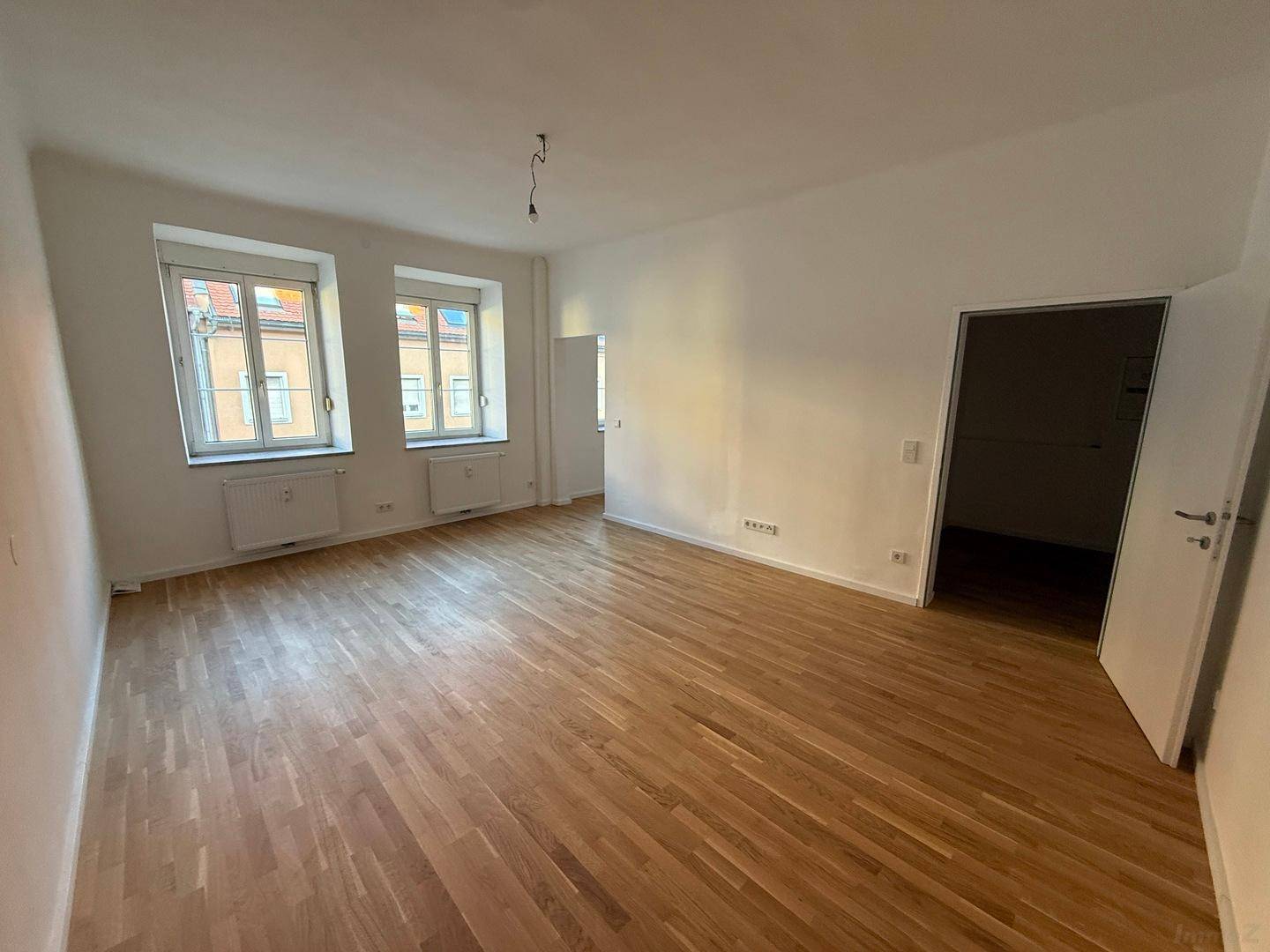 Geräumiges Zimmer mit Parkettboden, weißen Wänden und zwei Fenstern, ideal für Wohnzwecke.