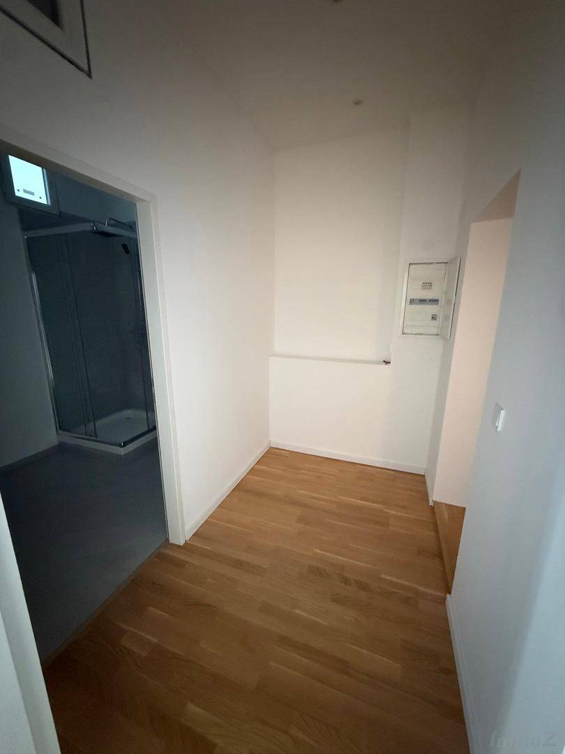 Heller Flur mit Parkettboden und Zugang zu einem modernen Badezimmer mit Dusche.