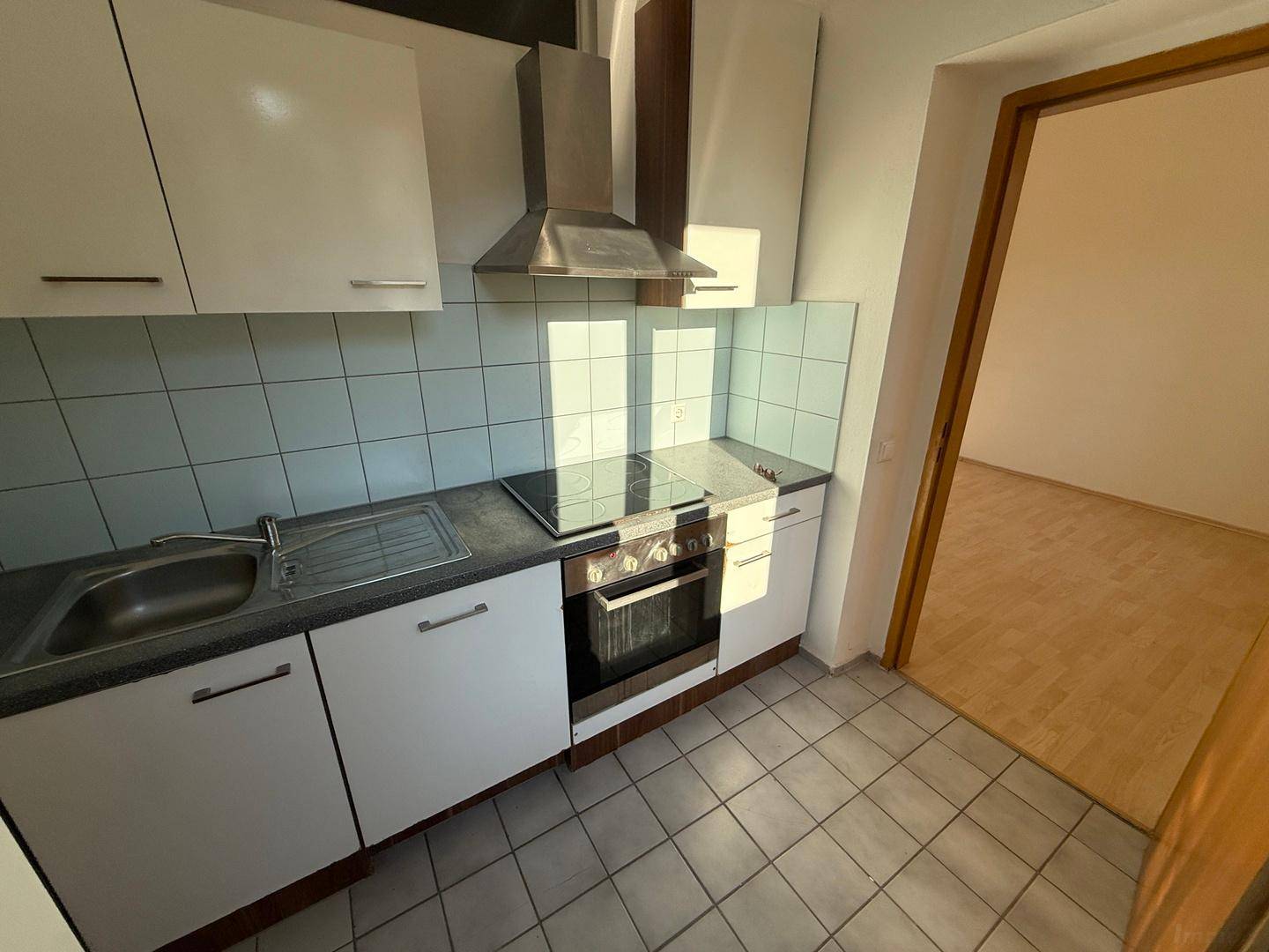 Kompakte Küche mit weißen Unterschränken, Spülbecken und Kochfeld, ideal für kleine Haushalte.