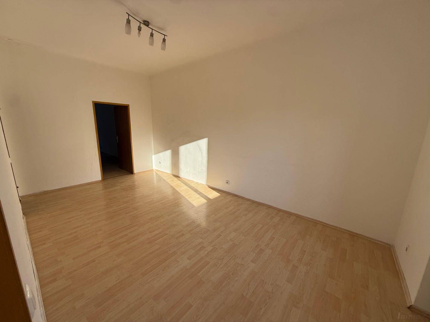 Helles, leeres Zimmer mit Laminatboden und Sonnenlicht, das durch die Fenster fällt.