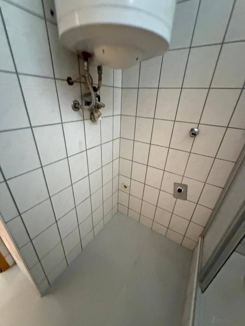 Geflieste Duschkabine mit weißem Boiler und einfachen Armaturen in einem Badezimmer.