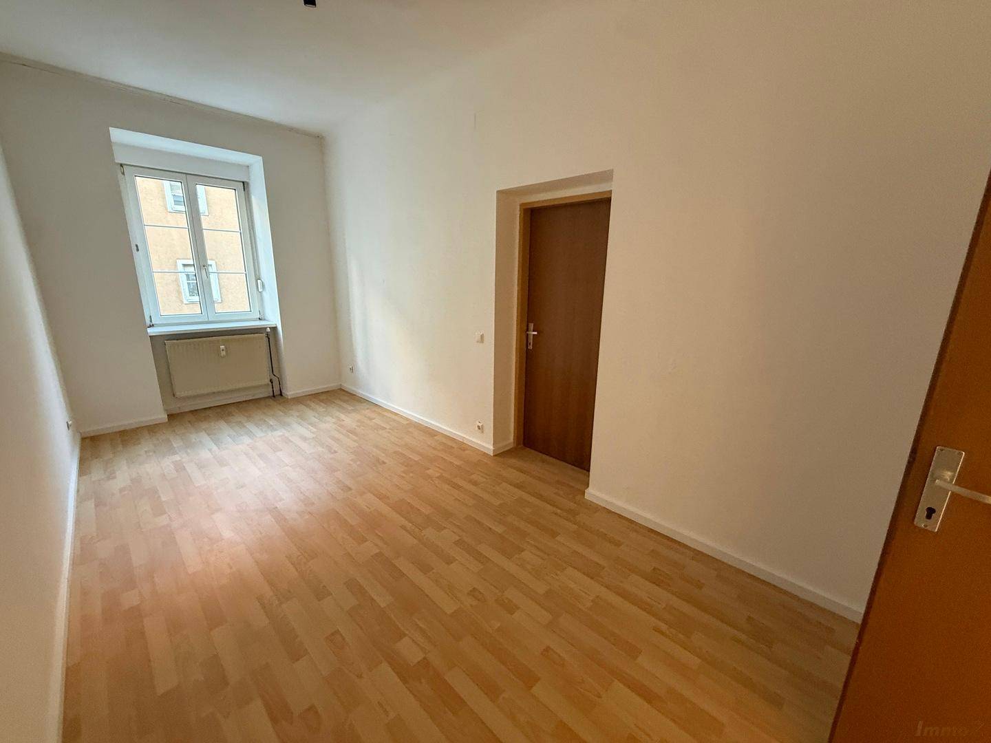 Leeres Zimmer mit Laminatboden und einem Fenster, das viel natürliches Licht spendet.