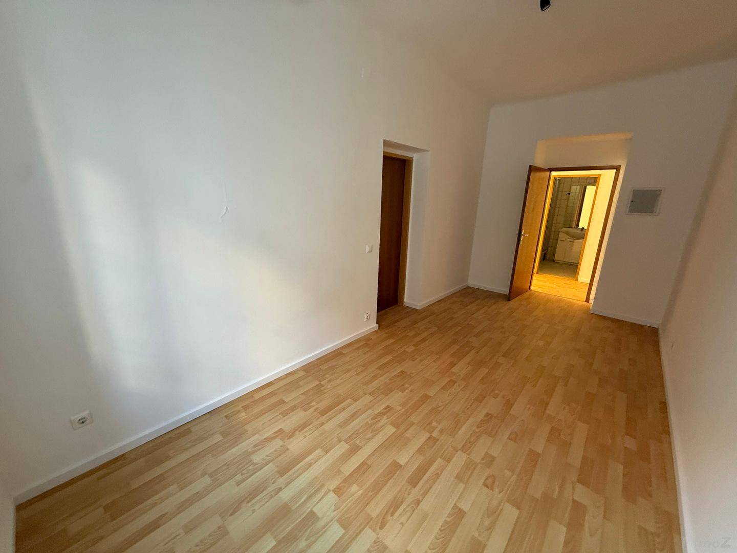 Leerer Raum mit Laminatboden und einer Tür, die zu einem gefliesten Badezimmer führt.