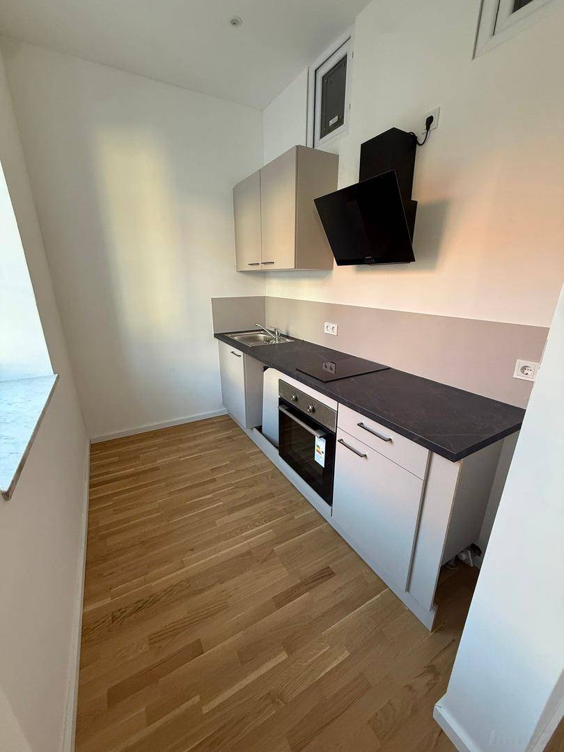 Kompakte Küchenzeile mit modernen Geräten und Holzboden, ideal für kleine Wohnungen.