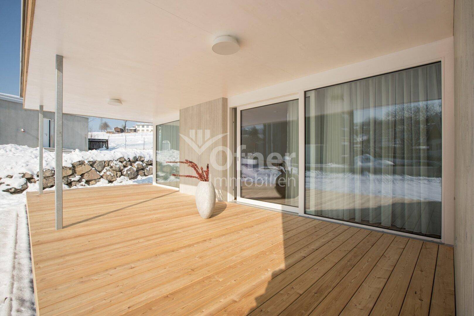 Überdachte Holzterrasse mit Blick auf die verschneite Landschaft und große Glasfronten.