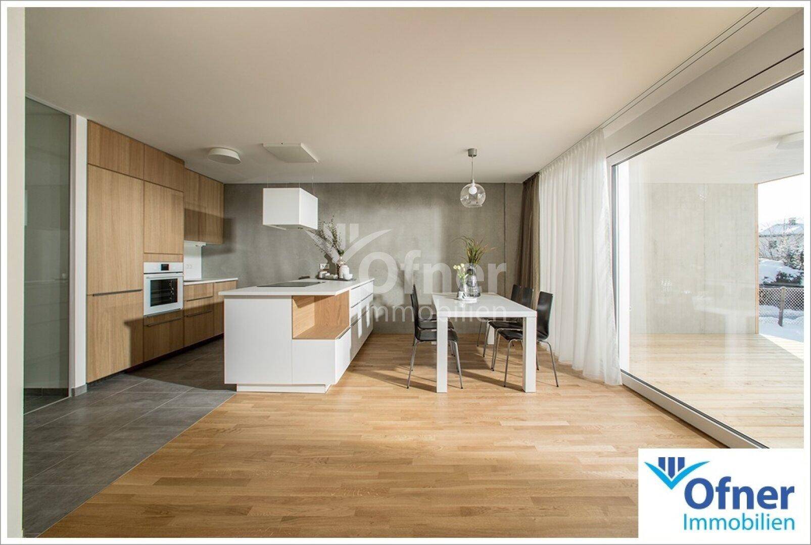 Moderne offene Küche mit Holzelementen, Kochinsel und Essbereich, verbunden mit der Terrasse durch große Fenster.