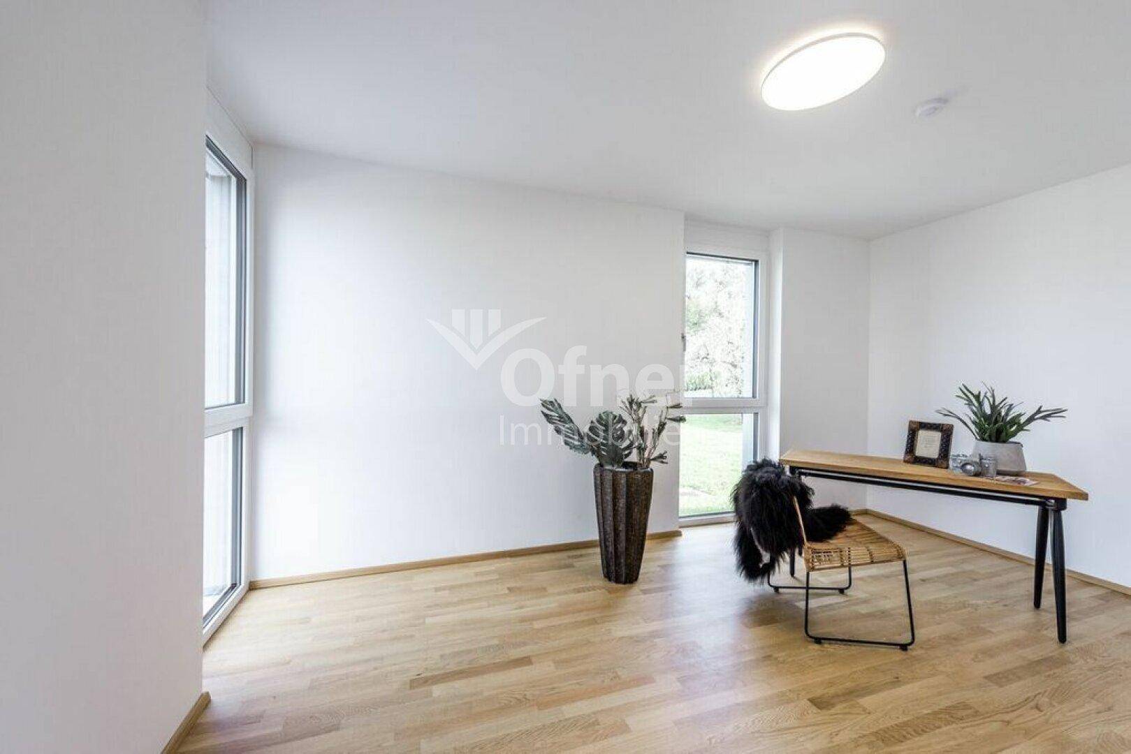 Helles Zimmer mit Holzboden, großem Fenster und modernem Schreibtischbereich.