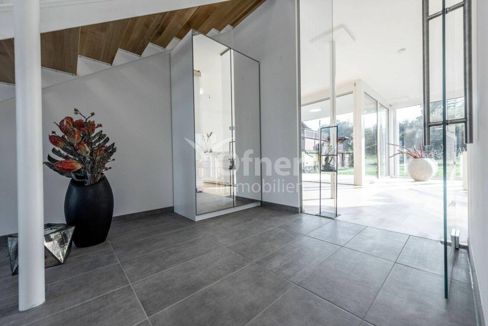 Moderner Eingangsbereich mit grauen Fliesen, offener Treppe und viel Tageslicht.