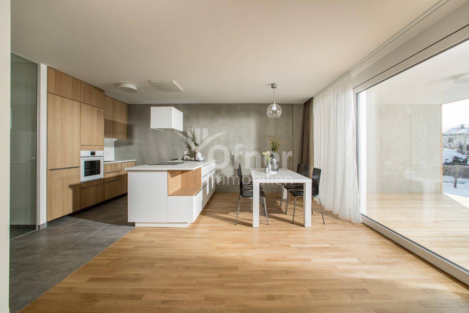 Moderne Einbauküche mit Holzfronten und weißer Insel, kombiniert mit Essbereich und Holzboden.