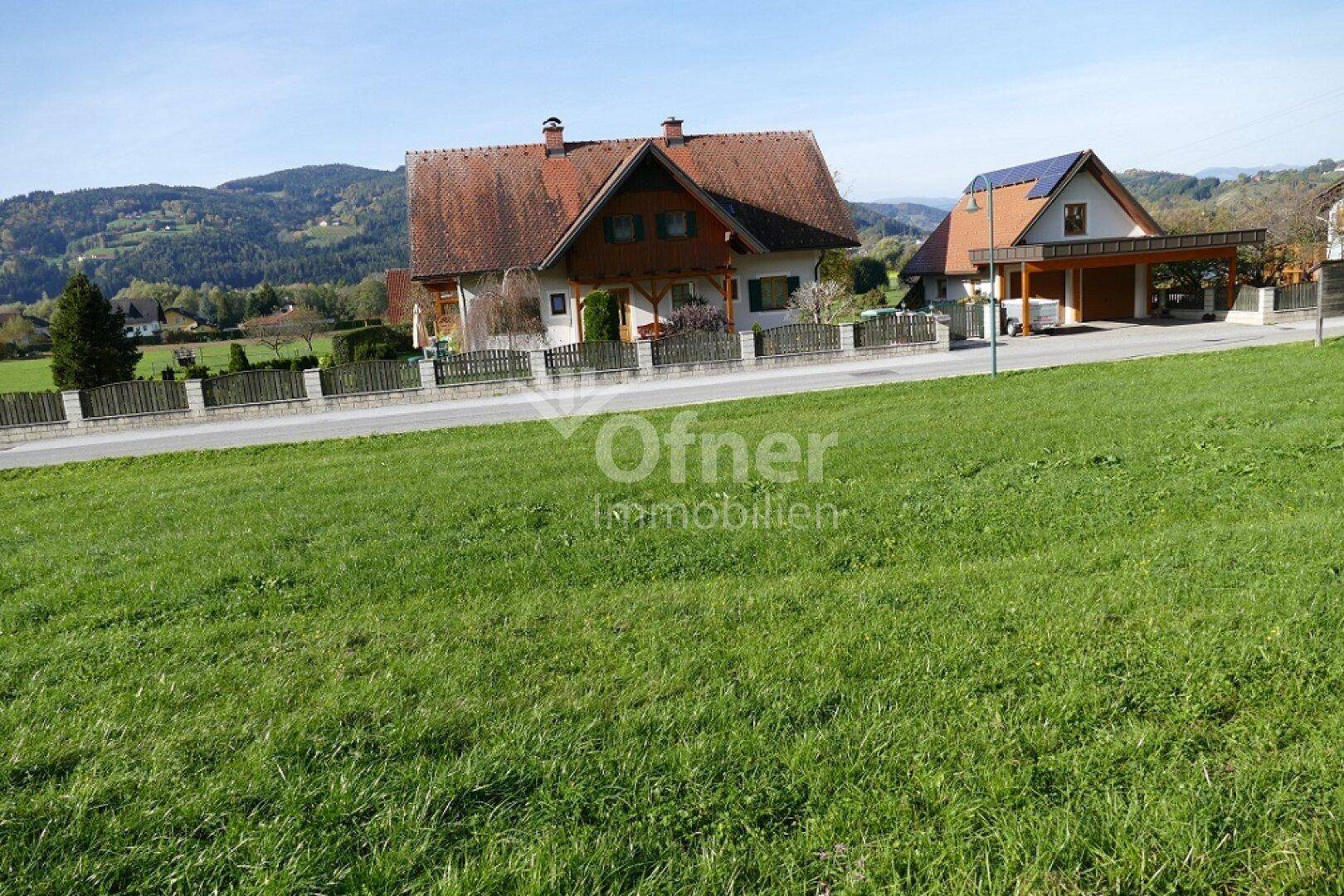 Offene Grünfläche mit Blick auf traditionelle Häuser und die umgebende Naturlandschaft.