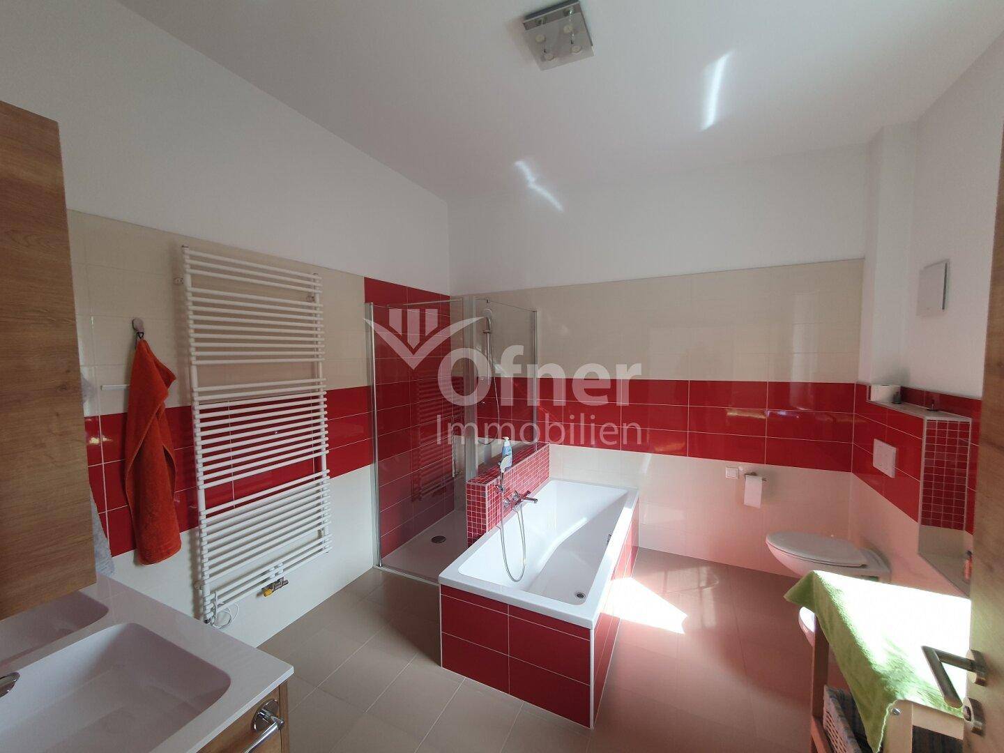 Modernes Badezimmer mit roten und weißen Fliesen, Badewanne, Dusche und Handtuchheizkörper.