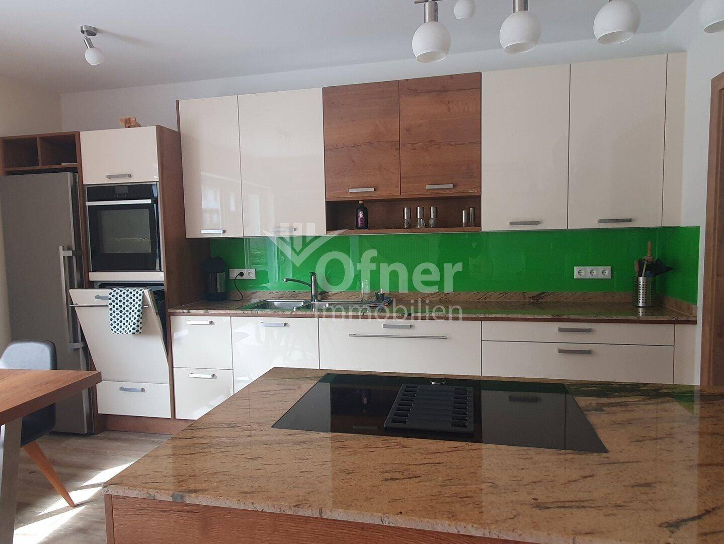 Moderne Einbauküche mit glänzenden Fronten, grüner Rückwand und Induktionskochfeld auf der Insel.