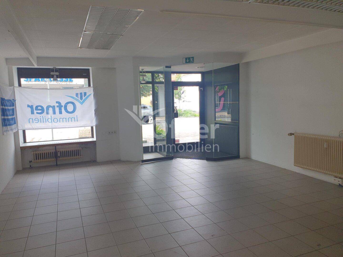 Eingangsbereich des Gewerberaums mit Glastür, Schaufenster und Fliesenboden.