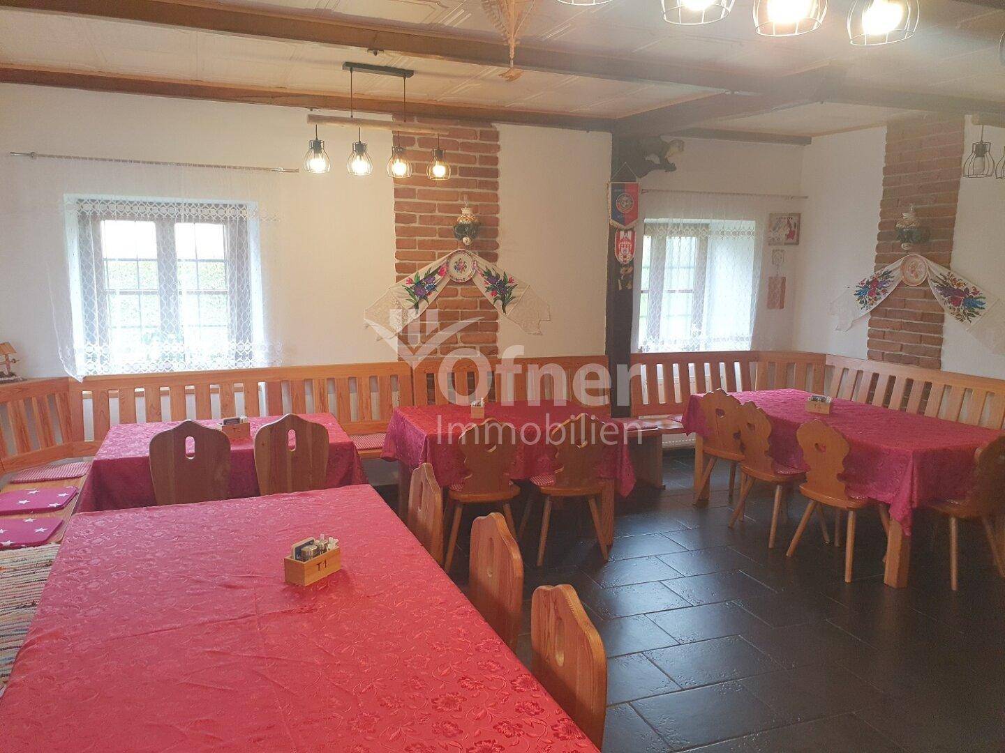 Gemütlicher Gastraum mit Holzbänken, roten Tischdecken und traditionellem Fliesenboden.