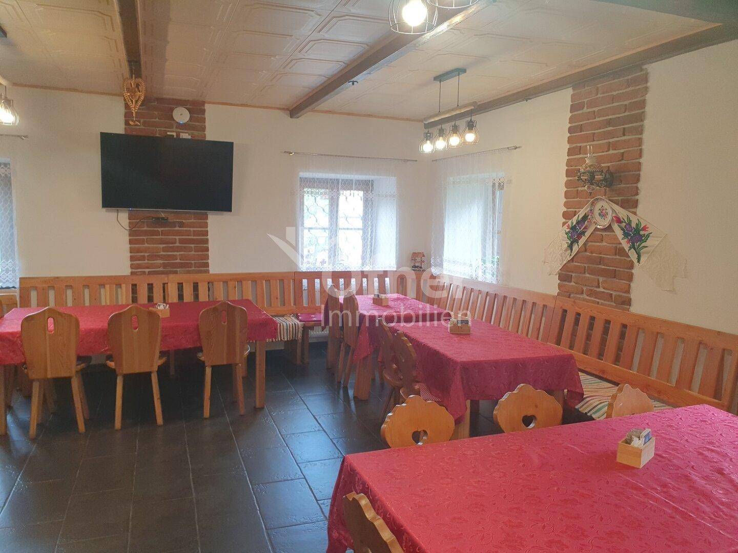 Heller Gastraum mit traditionellen Holzmöbeln, roten Tischdecken und Fliesenboden.